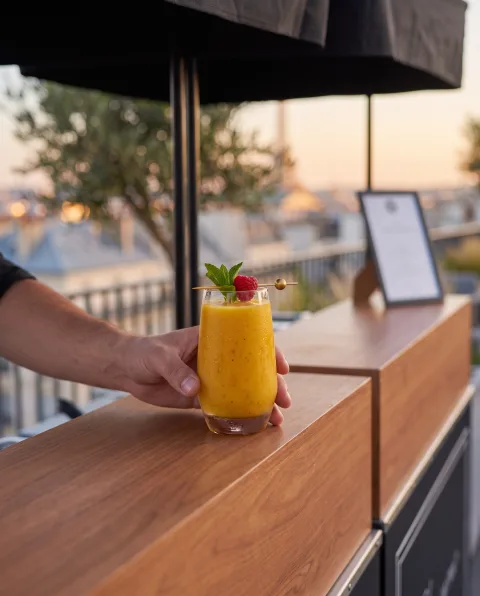 Smoothie mangue-framboise tenu à la main, toit-terrasse parisien